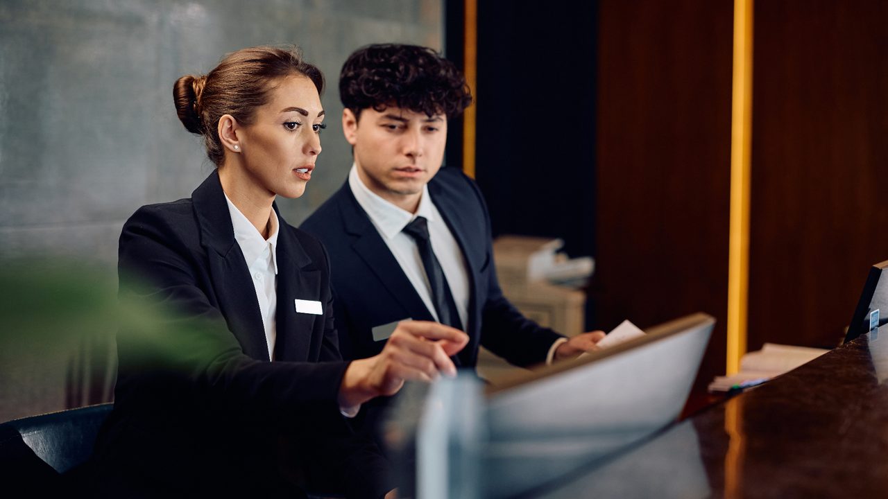 Two hotel receptionists collaborating at a front-desk workstation.