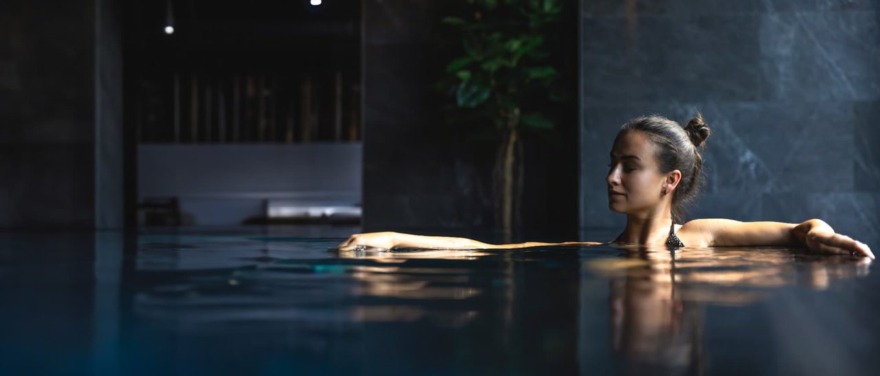 Guest resting at the edge of a dimly lit indoor spa pool