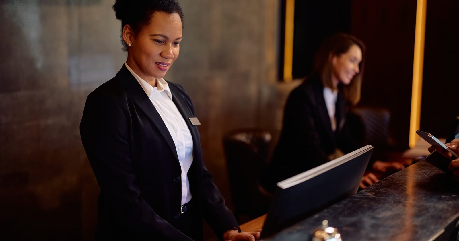 Hotel receptionist working at a front-desk computer while a guest pays at the counter
